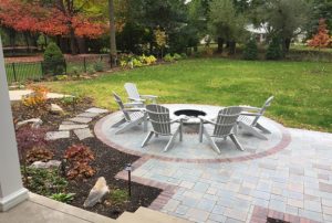 outdoor firepit surrounded by white chairs against lush green yard in the fall