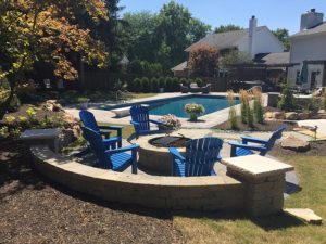 In-ground pool with blue chairs and firepit next to it